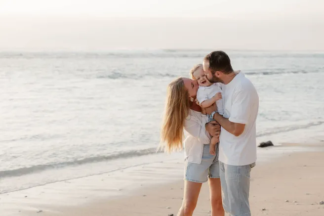 Au bord de l’eau, dans la lumière du soir, un couple embrasse sa fille qu’il tient entre eux