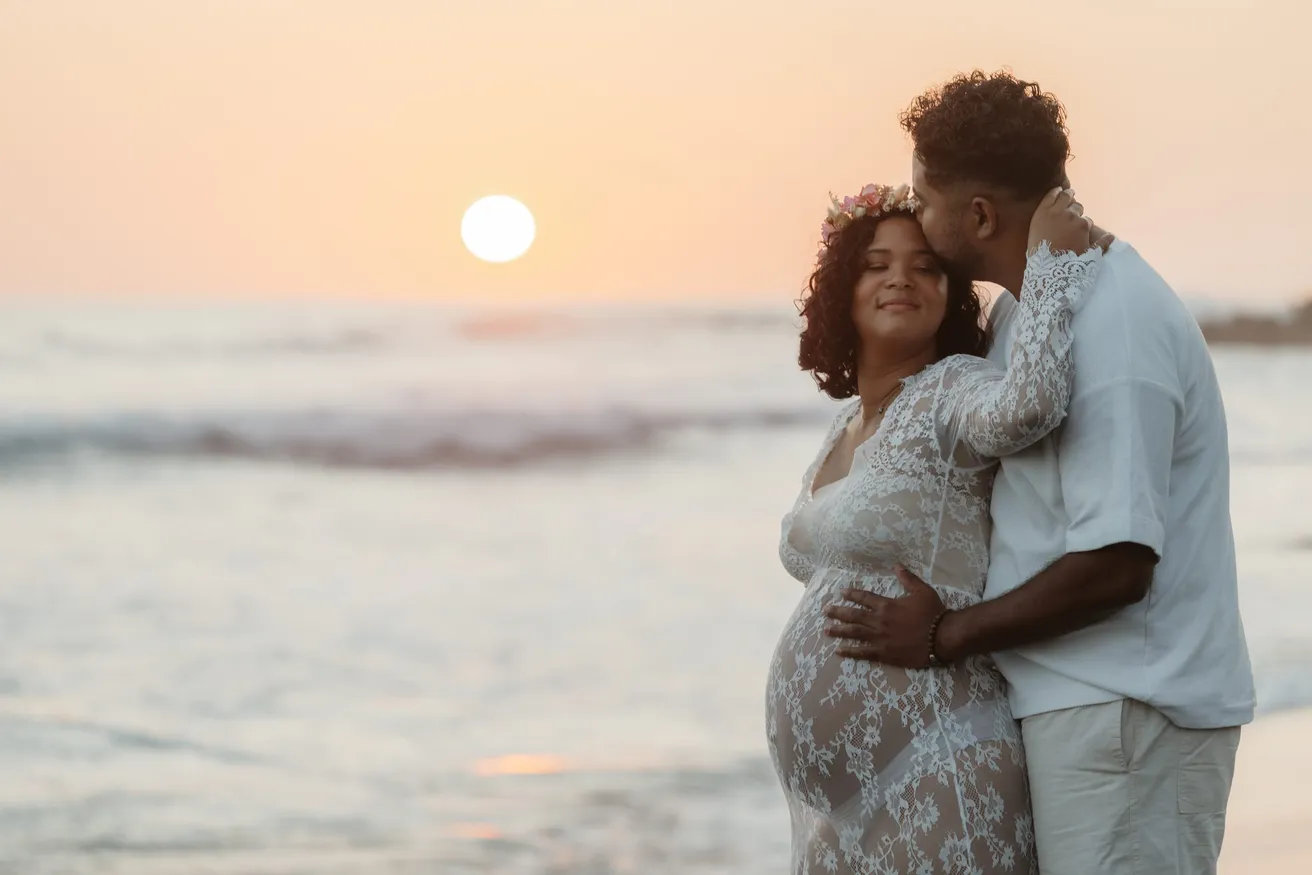 Le futur papa embrasse la future maman en dentelle blanche, soleil bas sur la mer