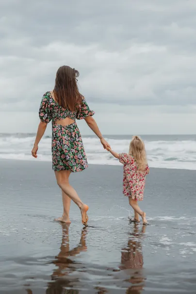 Une mère et sa petite fille marchent main dans la main sur le sable mouillé, face à la mer