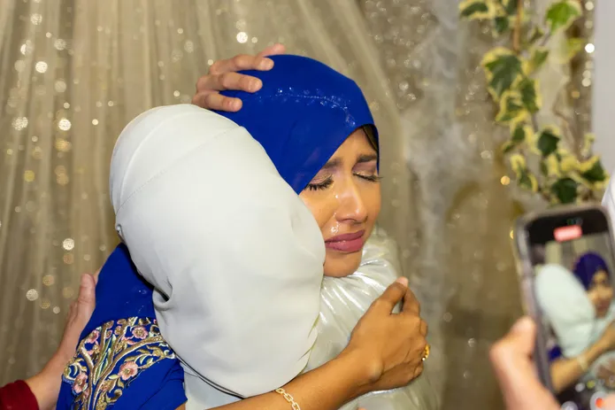 Une femme voilée de bleu serre dans ses bras une femme voilée de blanc, un téléphone filme la scène