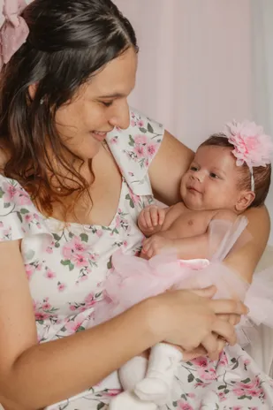 Une mère en robe fleurie sourit à son bébé en tutu, coiffé d’une fleur rose