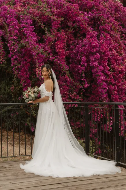 La mariée pose devant un mur de bougainvilliers fuchsia, voile déployé sur le ponton