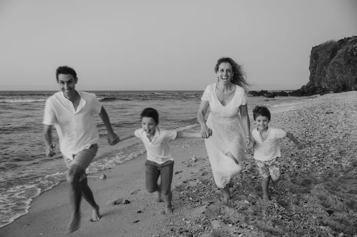 En noir et blanc, les parents courent sur la plage avec leurs deux garçons