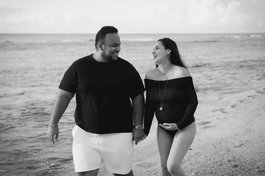 En noir et blanc, un couple marche main dans la main dans les vagues en souriant