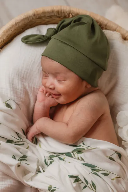 Nouveau-né endormi, bonnet vert noué, sur une couverture à feuillages