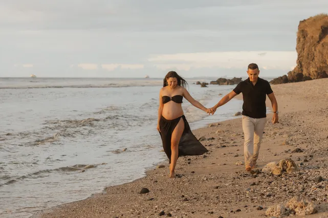Un couple qui marche main dans la main au bord de l’eau, au pied d’une falaise