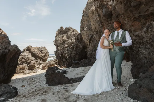 Les mariés posent entre les rochers volcaniques d’une plage