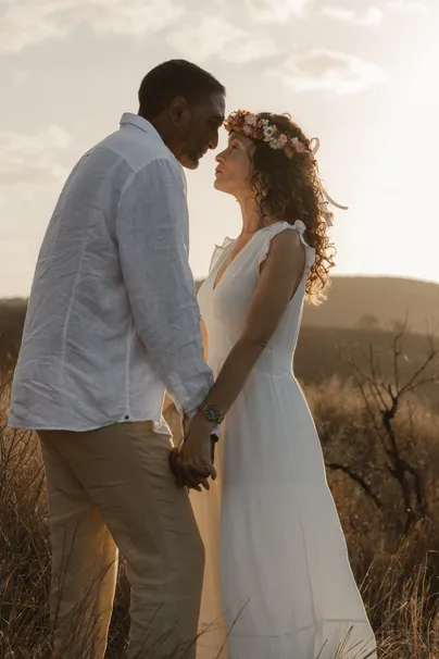 Les mariés se tiennent les mains, front contre front, la mariée couronnée de fleurs
