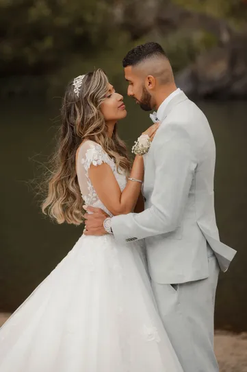 Les mariés enlacés au bord d’un bassin, la mariée aux longs cheveux ondulés en robe de dentelle