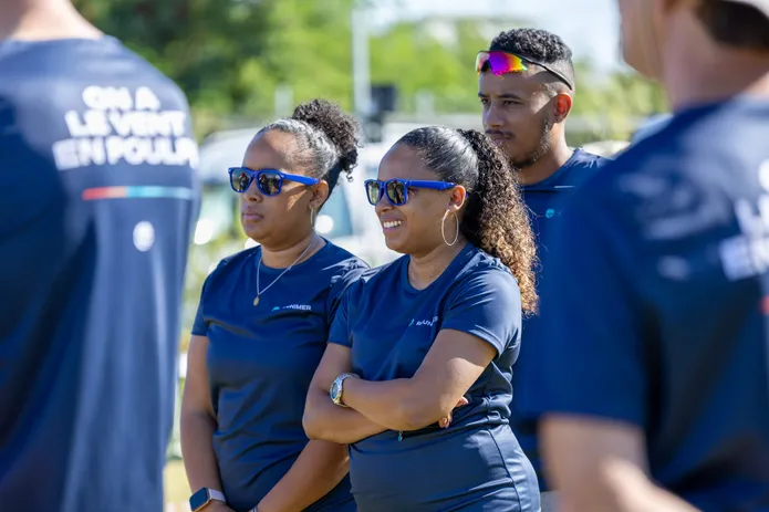 Trois coéquipières en tee-shirts bleus et lunettes de soleil, les bras croisés, pendant un team building