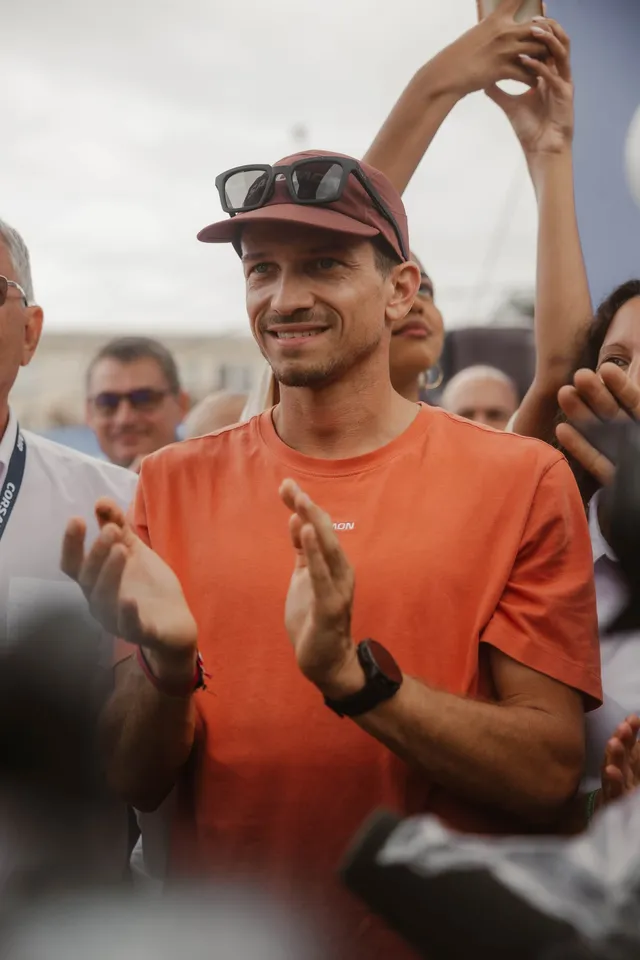Un spectateur en casquette et tee-shirt orange applaudit, souriant, au milieu de la foule