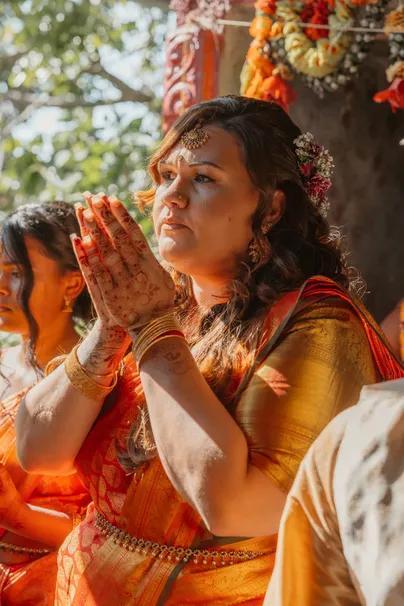 Femme en sari orange et doré, mains jointes ornées de henné, pendant la cérémonie