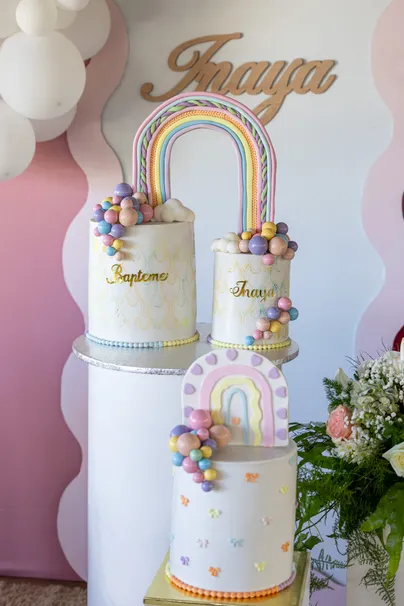 Un gâteau à étages aux arcs-en-ciel pastel, sous le prénom de l’enfant en lettres dorées