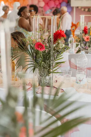 Une table décorée de fleurs rouges et de bougies, derrière des palmes au premier plan