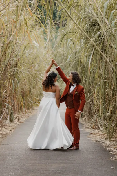 Les mariés dansent sur un chemin bordé de hautes herbes, robe blanche et costume rouille