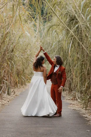Les mariés dansent sur un chemin bordé de hautes herbes, robe blanche et costume rouille
