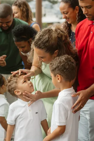 Une femme pose la main sur le front de deux petits garçons en polo blanc, entourés de leur famille