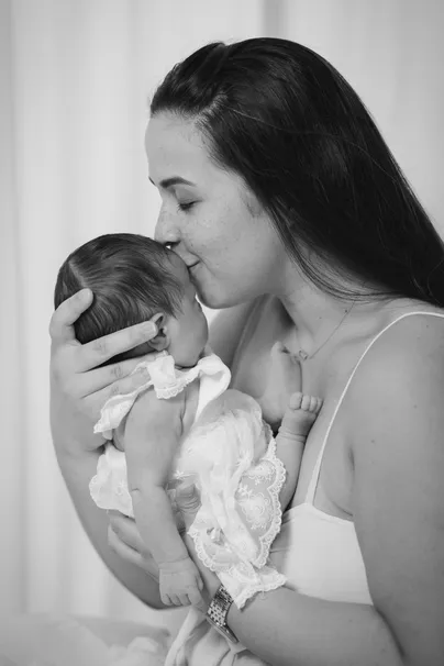 En noir et blanc, une maman embrasse le front de son nouveau-né blotti contre elle