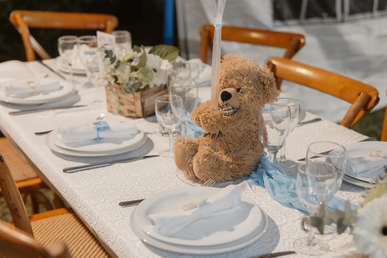 Une table dressée pour la fête, un ours en peluche assis entre les assiettes et les verres