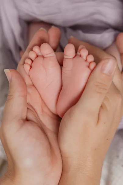 Gros plan sur les pieds d’un nouveau-né au creux de deux mains d’adulte