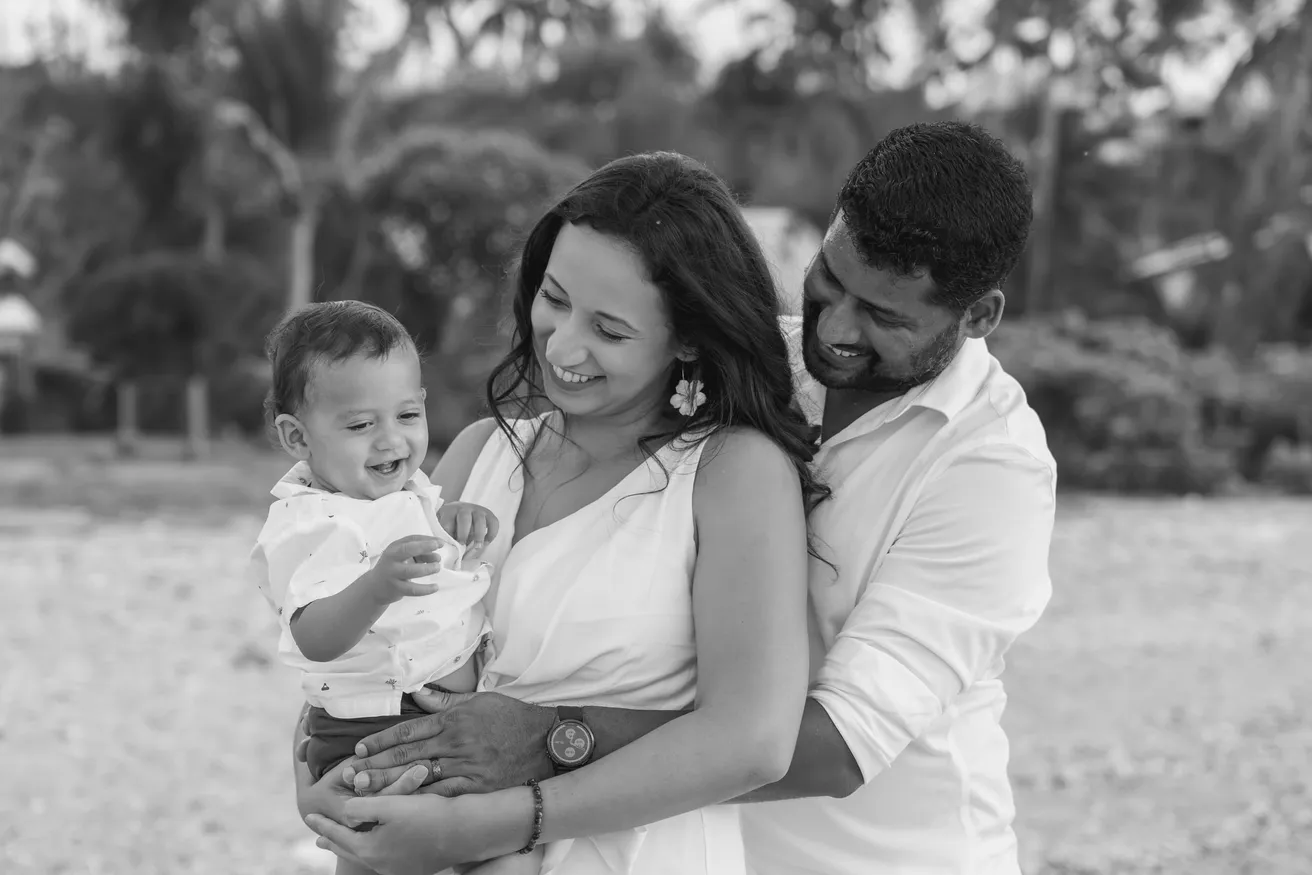 En noir et blanc, un couple sourit à son petit garçon que la mère porte, sous les palmiers