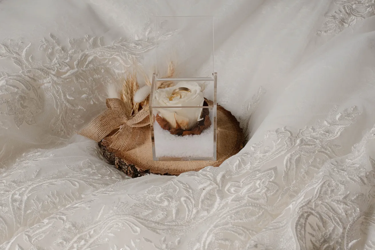 Boîte à alliances en verre sur une rondelle de bois, posée dans la dentelle de la robe