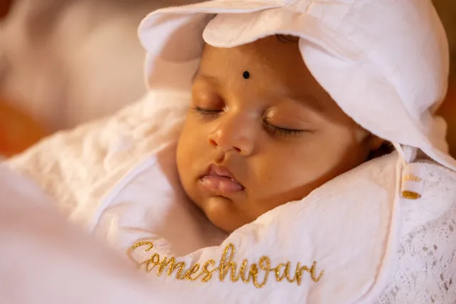 Un bébé endormi coiffé d’un bonnet blanc, son prénom brodé en fil doré sur l’étole
