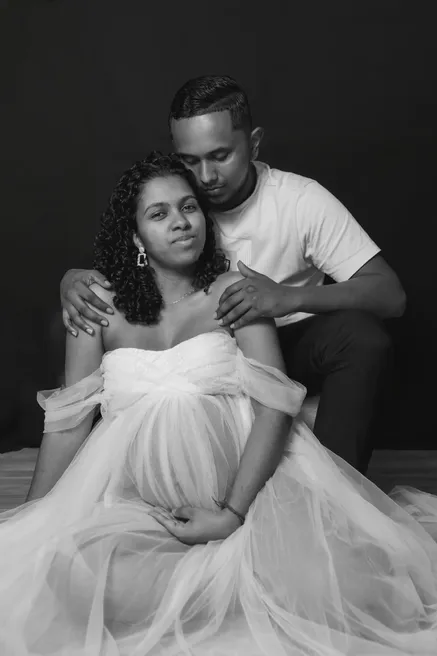 En noir et blanc, un couple en studio, la future maman assise dans une robe de tulle