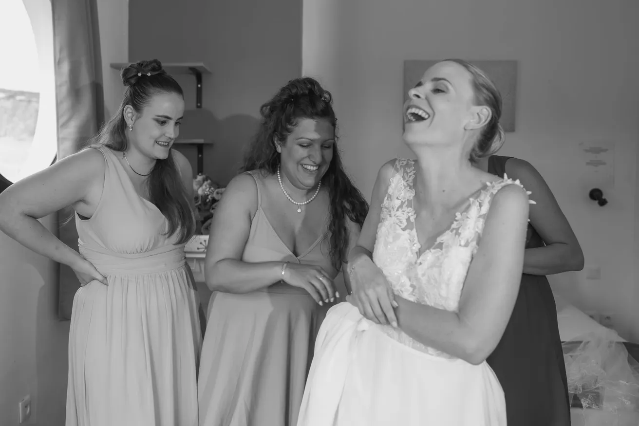 En noir et blanc, la mariée rit avec ses demoiselles d’honneur pendant les préparatifs