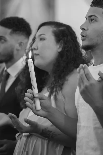 En noir et blanc, une jeune femme tient un cierge allumé, entourée de proches pendant la cérémonie
