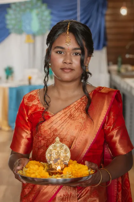 Une jeune femme en sari rouge et or tient un plateau d’offrandes avec une lampe à huile
