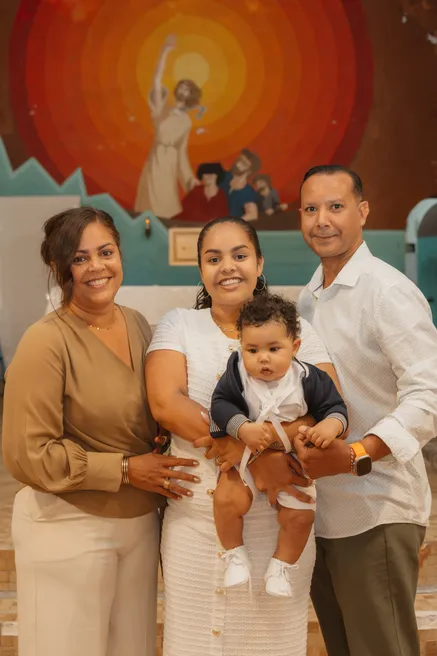 La famille pose avec l’enfant devant une fresque religieuse aux tons orangés, dans l’église
