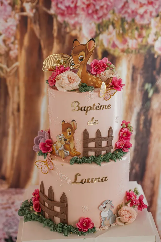Un gâteau de baptême à étages décoré de Bambi et de fleurs, au prénom de l’enfant