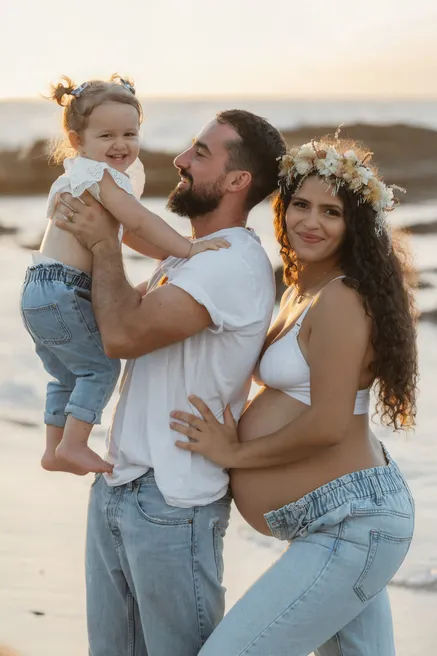 Un couple et leur petite fille au bord de la mer, la future maman couronnée de fleurs