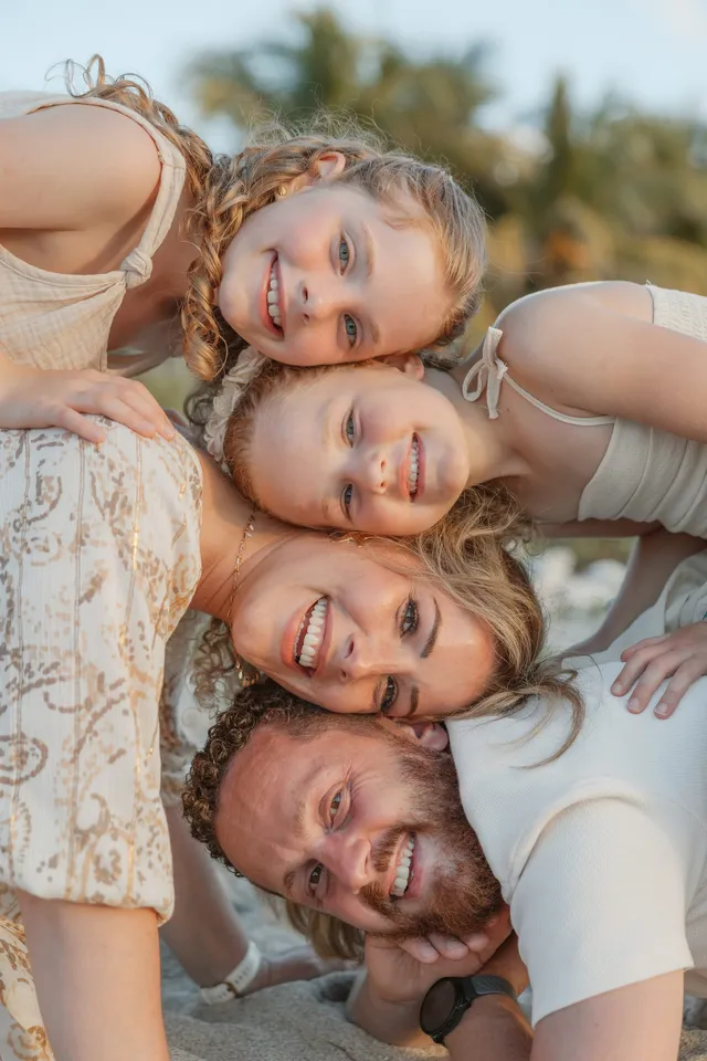Vus de dessus, parents et enfants allongés tête contre tête sur le sable, tous souriants