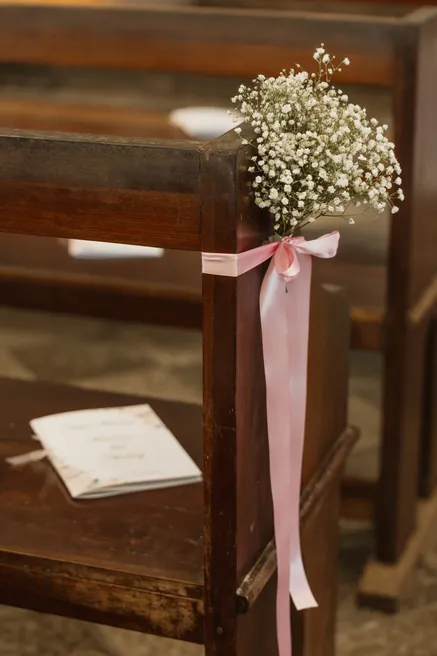 Bouquet de gypsophile noué d’un ruban rose au bout d’un banc d’église, livret posé sur le banc