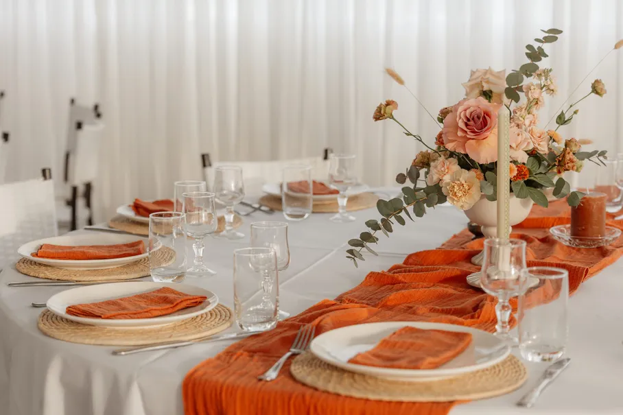 Longue table de réception aux serviettes orange et verres ciselés, fleurs pêche au centre