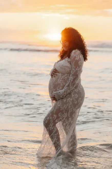Future maman en dentelle transparente dans l’eau, en contre-jour du soleil couchant