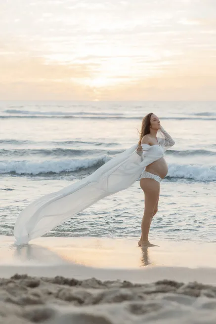 Future maman sur la plage, la traîne de sa robe emportée par le vent