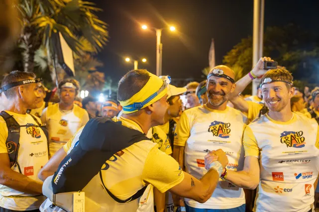 De nuit, des coureurs de trail en tee-shirts jaunes s’encouragent sous les lampadaires avant le départ