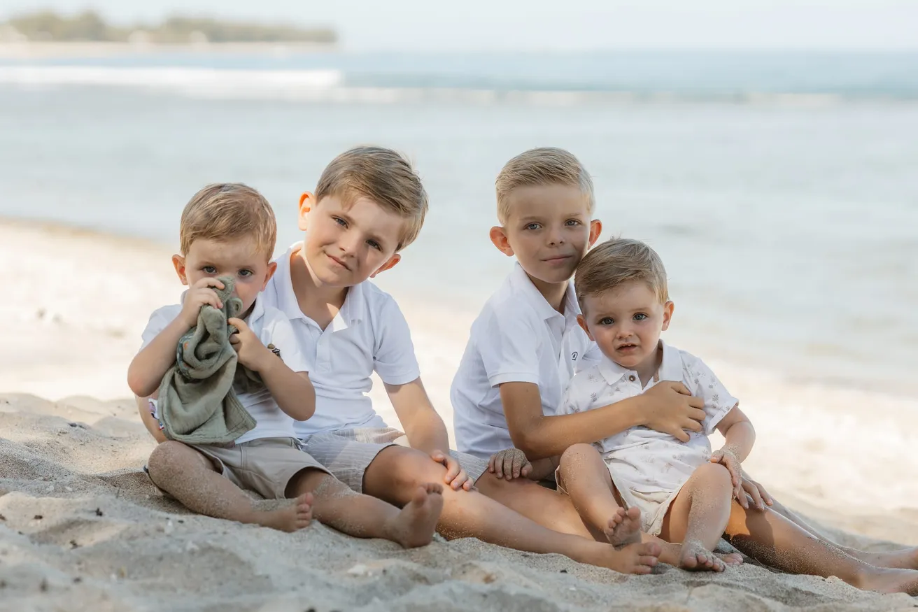 Quatre petits garçons en chemises blanches assis côte à côte sur le sable