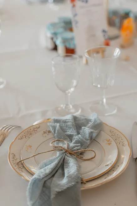 Assiette ancienne à liseré doré, serviette bleue nouée de ficelle et verres ciselés
