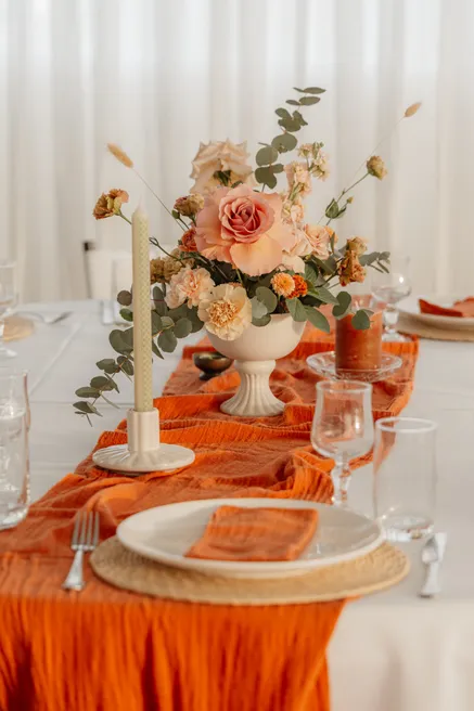 Table dressée d’un chemin orange, d’une bougie et d’une coupe de roses pêche