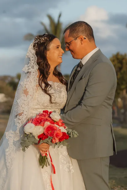 Les mariés se regardent en souriant, la mariée en voile de dentelle et bouquet rouge