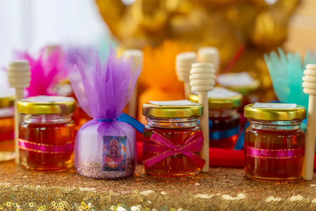 Petits pots de miel décorés de rubans roses et de tulle coloré, avec leurs cuillères en bois