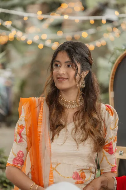 Invitée en tenue indienne orange et crème, collier doré, sous des guirlandes lumineuses