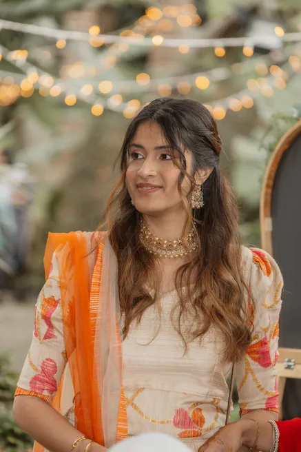 Invitée en tenue indienne orange et crème, collier doré, sous des guirlandes lumineuses