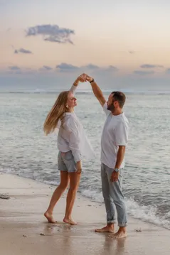 Un couple danse les pieds dans l’eau, bras levés pour une pirouette sous le ciel du soir