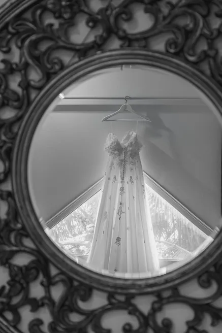 En noir et blanc, la robe de mariée suspendue, vue à travers un miroir rond en fer forgé