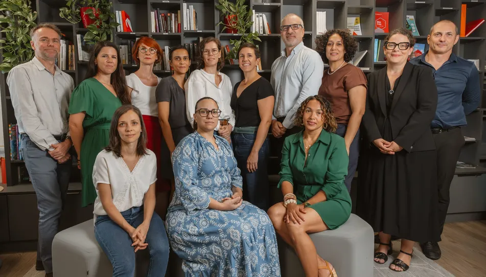 Une équipe d’une vingtaine de personnes pose, assise et debout, dans une bibliothèque
